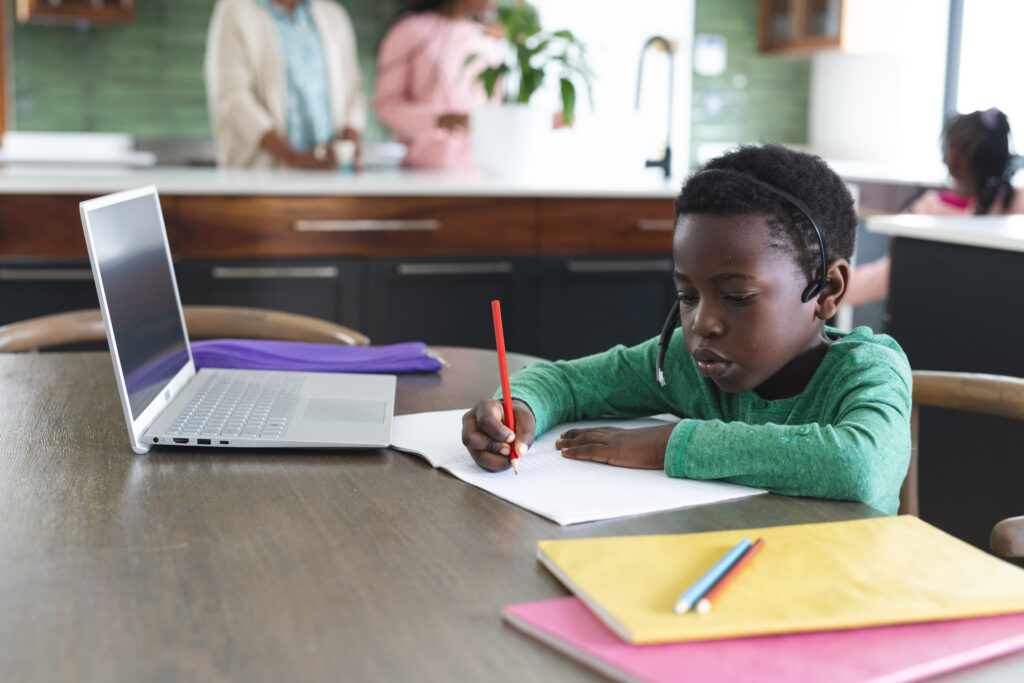 Young African boy studying coding classes for kids using a laptop and writing note